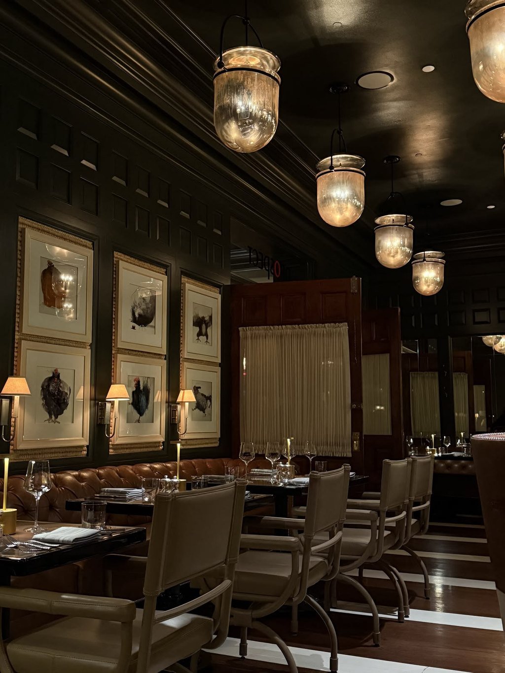 A dark paneled dining room set for dinner under glass pendant lights