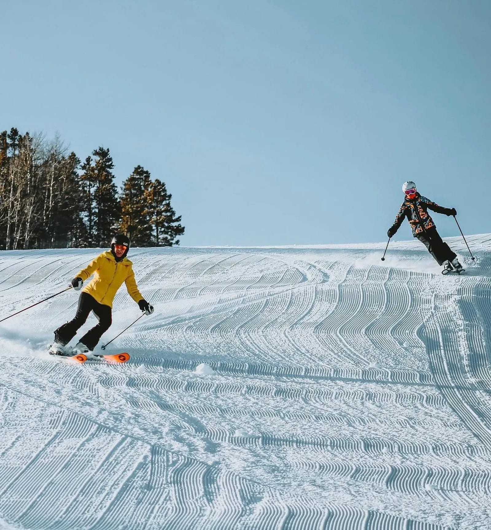 Two skiers making turns on a groomed mountain run
